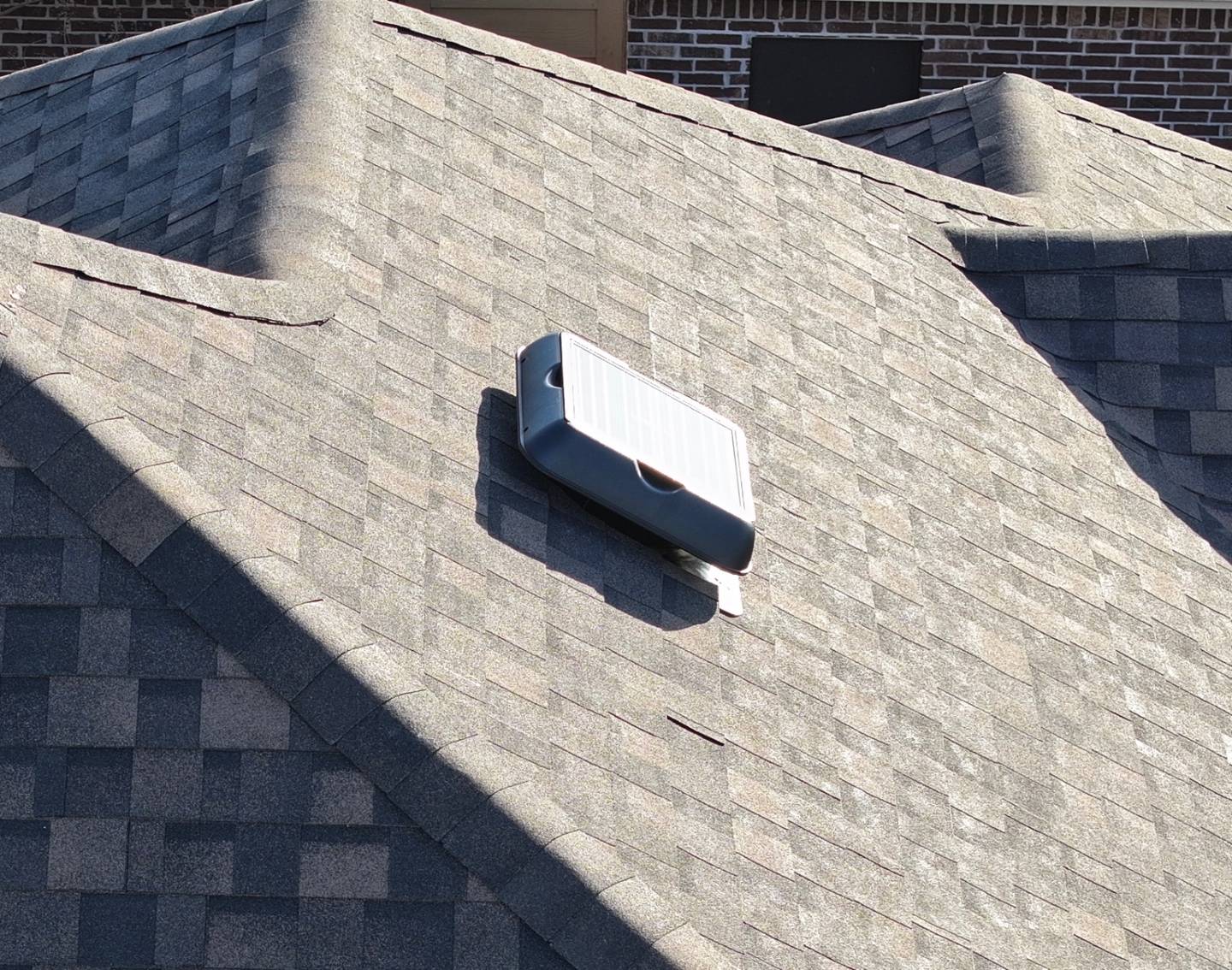 A solar-powered attic fan installed on a brown shingle roof, its solar panel angled toward the sun.
