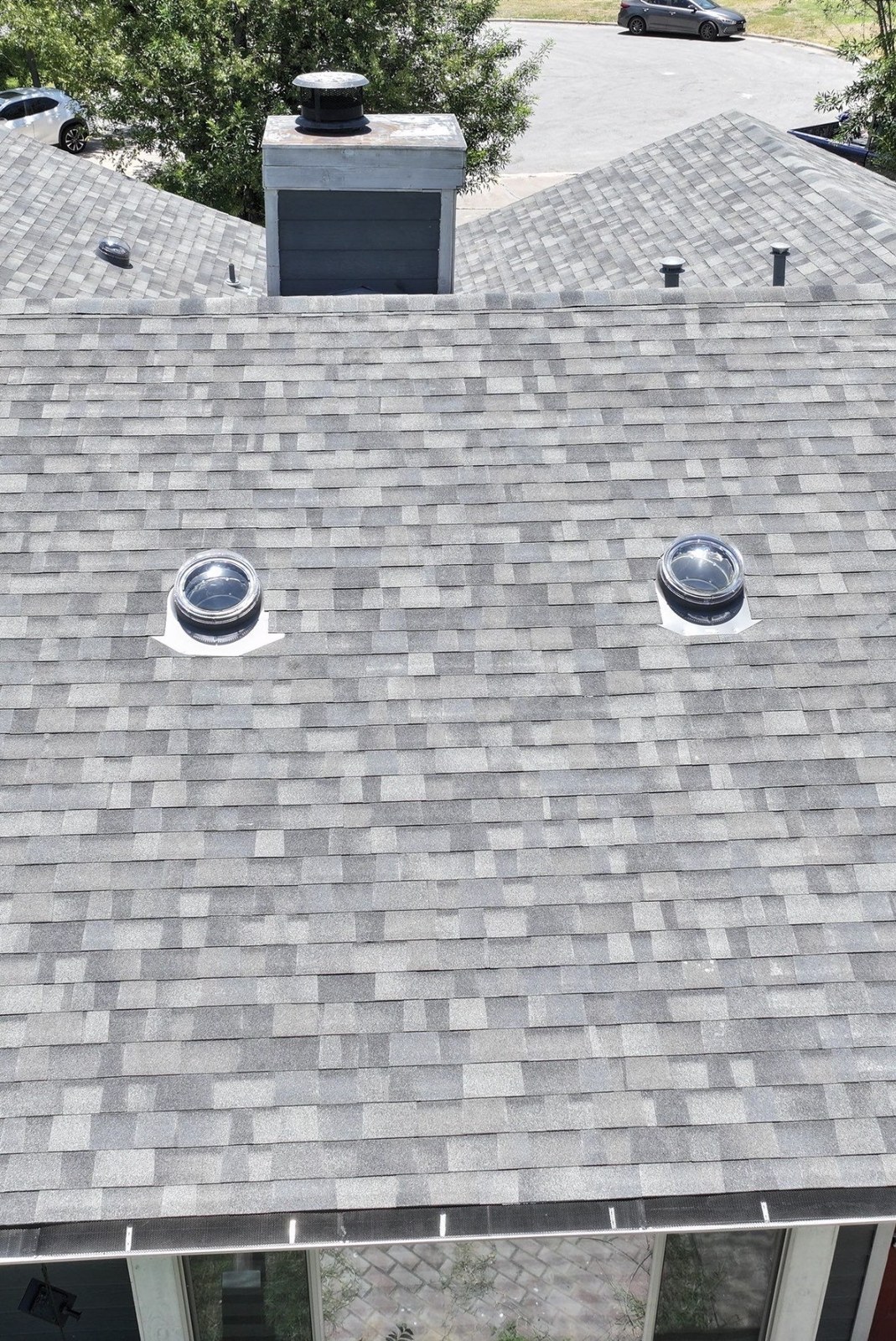 Aerial view of a gray shingle roof in Round Rock with two solar tube domes installed side by side.