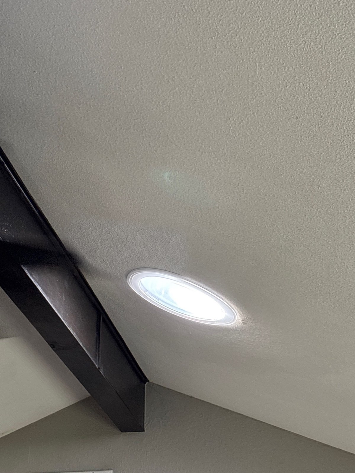 A round solar tube lens glowing with daylight in a sloped ceiling next to a dark wood beam.