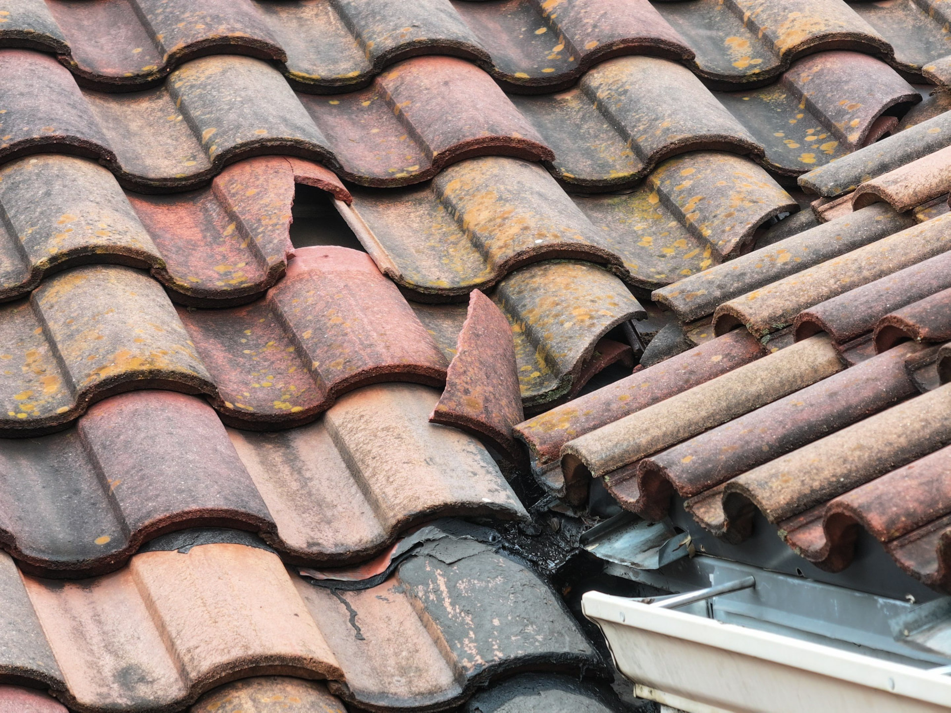 Broken and displaced clay roof tiles near a roof valley and gutter