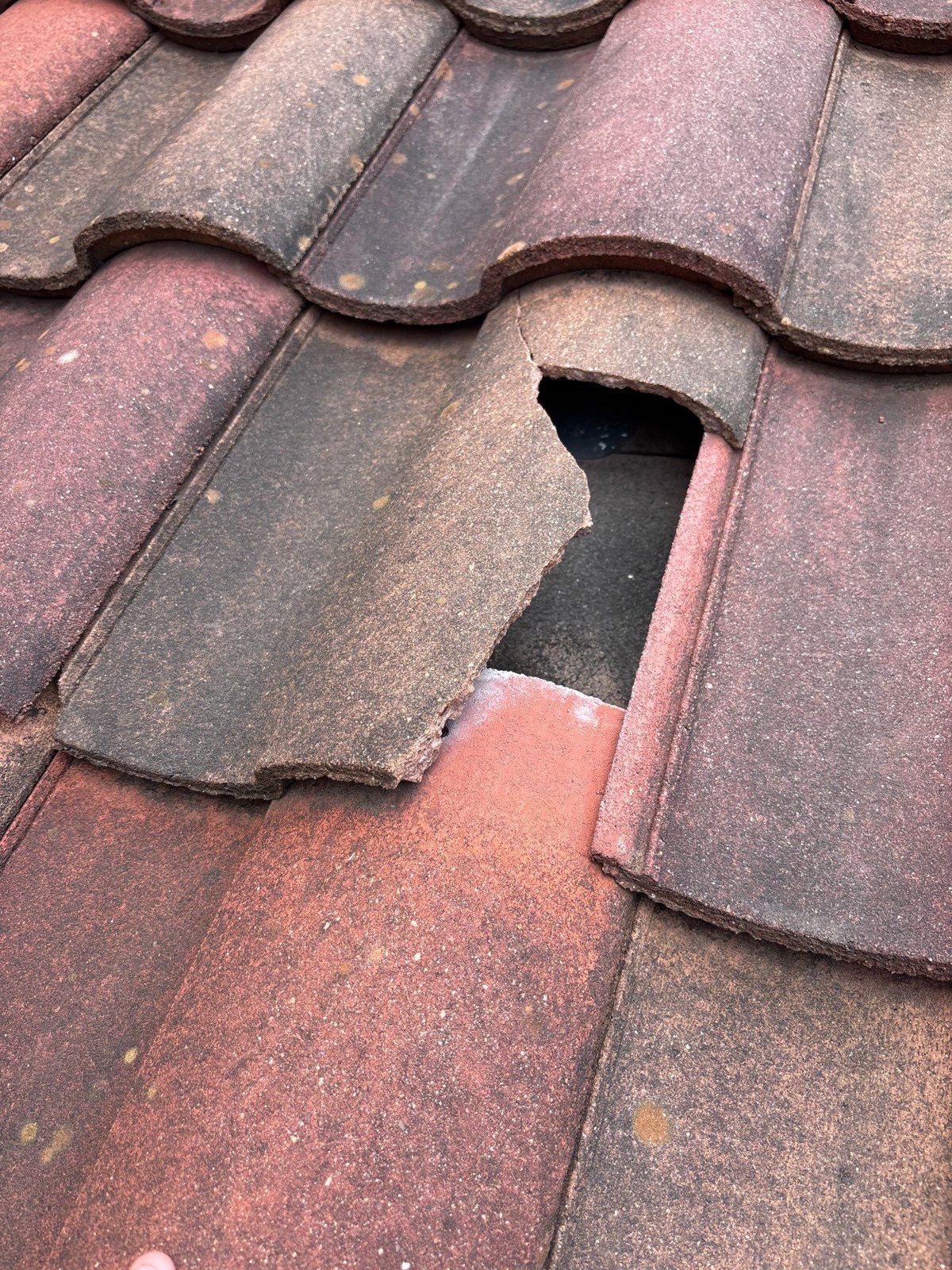 Close-up of a broken concrete tile with a hole that lets rain reach the layers underneath.