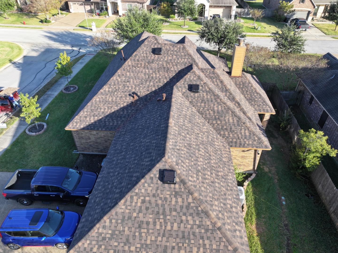 Aerial view of a brown shingle roof with three solar attic fans installed on different slopes.