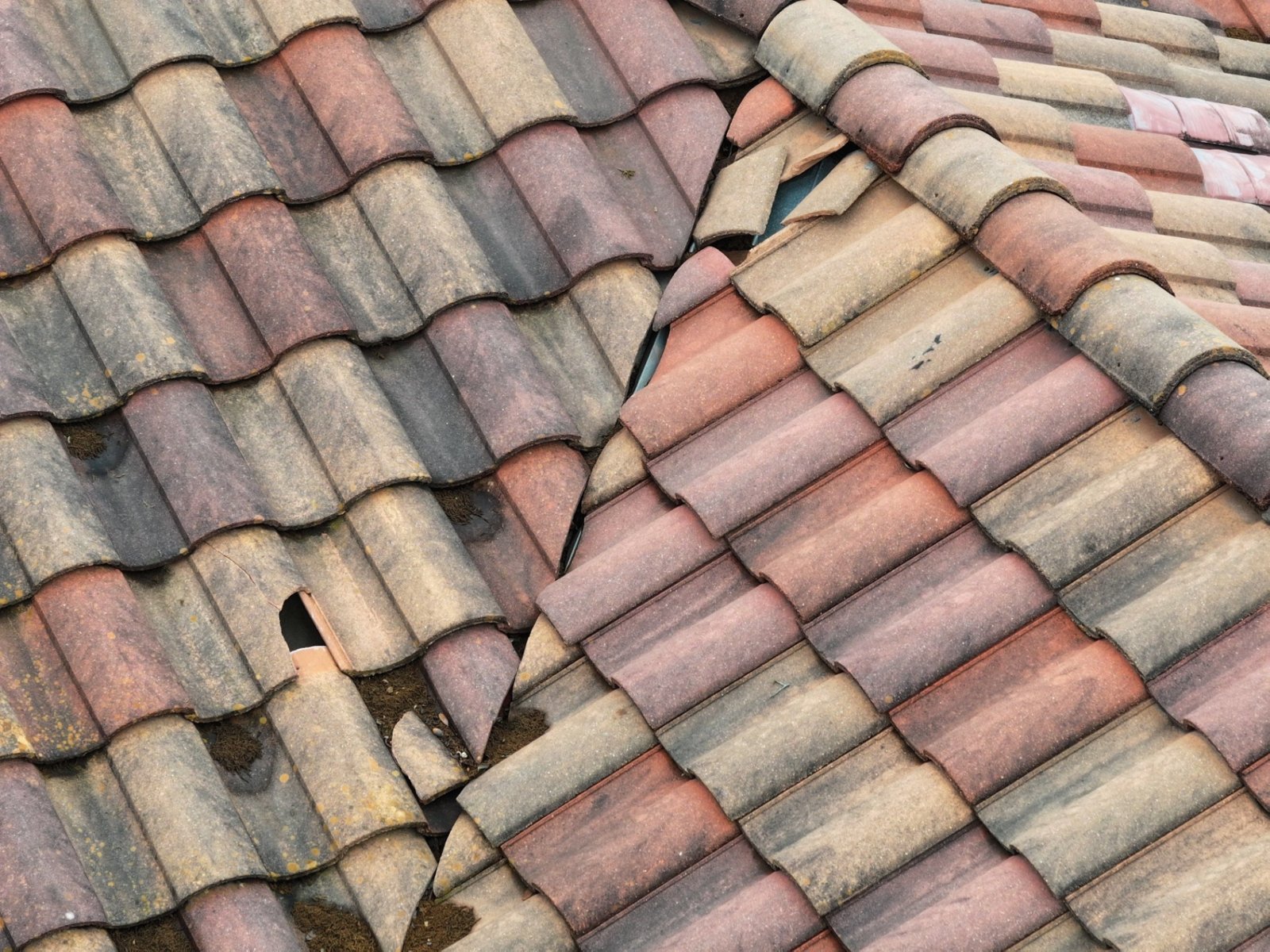 Broken tiles along a valley, exposing the metal valley flashing below.