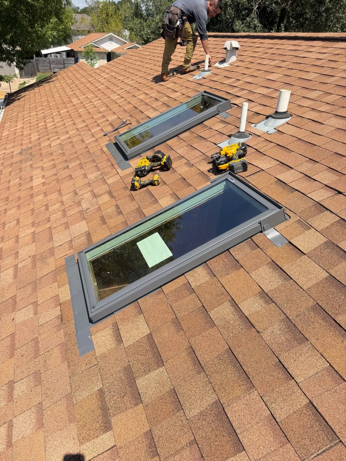 Two new skylights installed in a brown shingle roof, with a crew member working near the ridge.