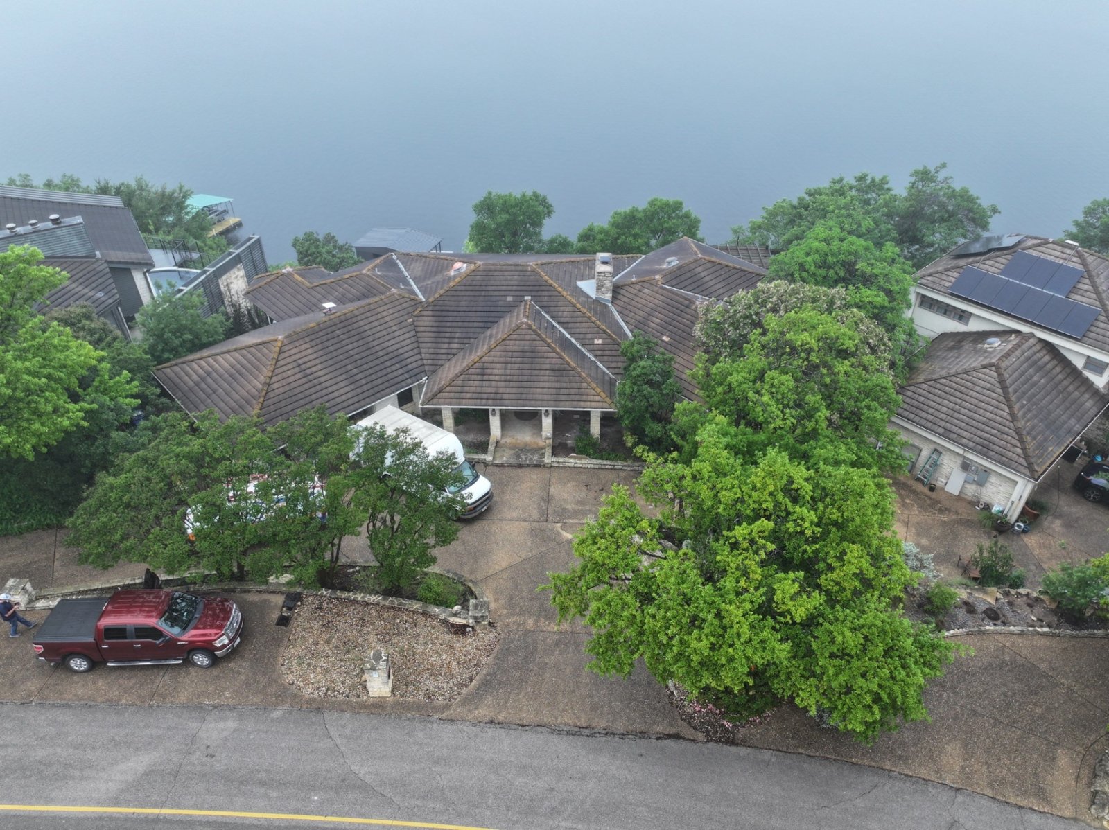 Aerial view of a Lakeway home on Lake Travis with its original weathered concrete tile roof, before replacement.