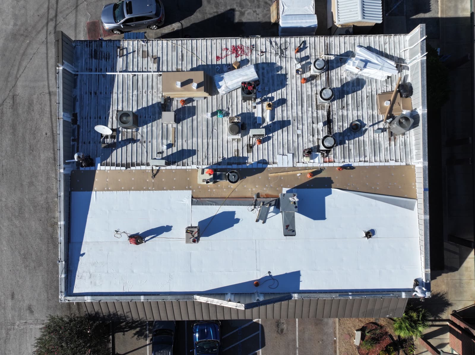 Aerial view of a restaurant roof mid-project: old metal roof at the top, fastened insulation board in the middle and new white PVC membrane at the bottom.